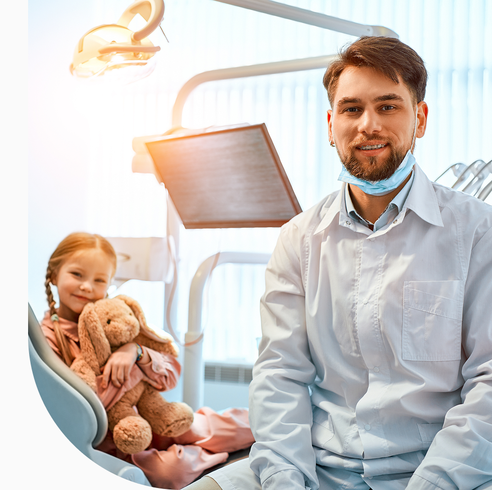 Male dentist with a young girl holding a teddy bear in a dental chair